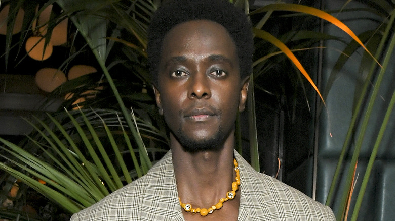 Edi Gathegi standing near plants