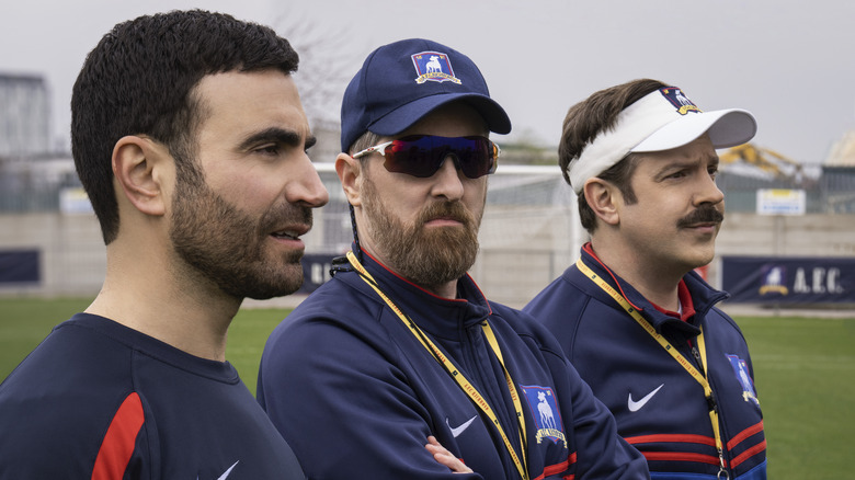 Roy Kent, Coach Beard, and Ted Lasso stand on a football pitch