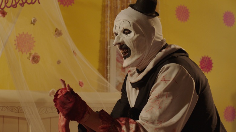 Art the Clown holds the bloodied hand of someone below frame