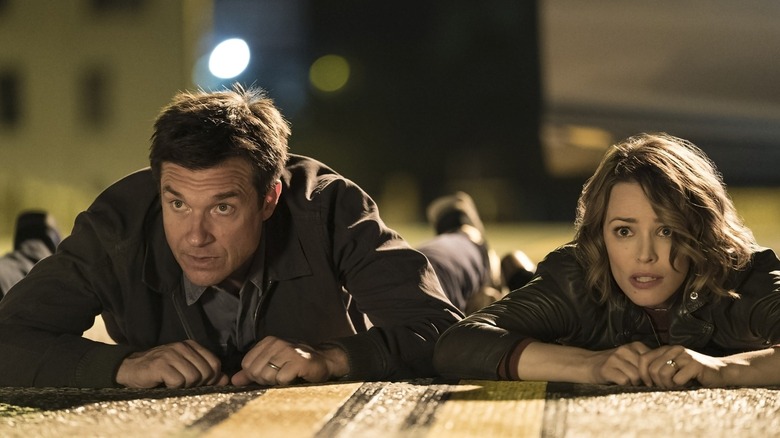 Max and Annie laying on the ground looking at something and worried in Game Night