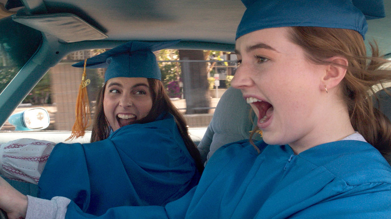 Molly and Amy wearing graduation robes and caps in a car in Booksmart