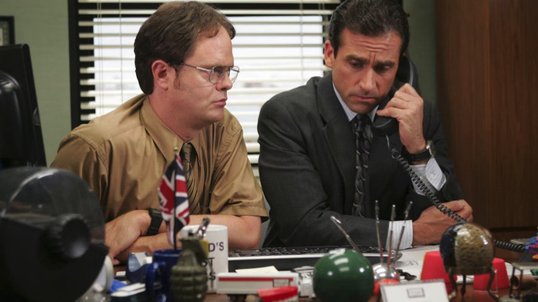 Dwight sits next to Michael on the phone