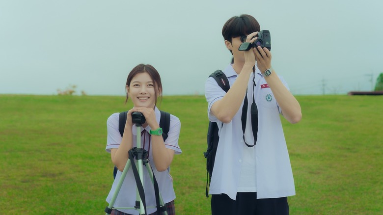 Hyun-jin and Bo-ra stand in a field with a camera and a tripod in "20th Century Girl" (2022)