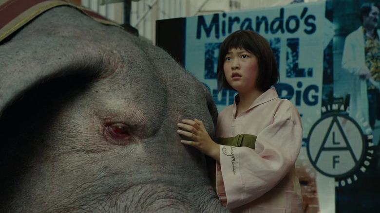 Mija puts her hand on the head of a giant pig and looks out into the distance with worry in "Okja" (2017)