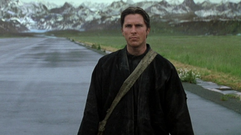 Bruce Wayne walking along a road in front of mountains in "Batman Begins"