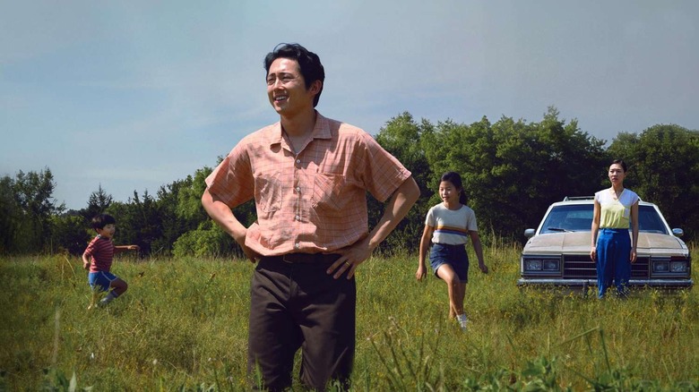 Jacob standing in a field with his family and car behind him in Minari