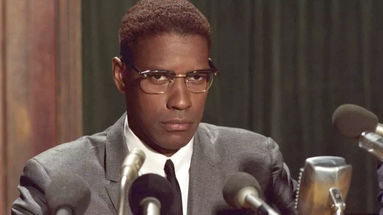 Malcolm X stands at a podium surrounded by microphones.