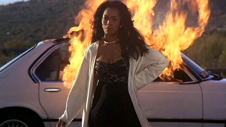 Angela Bassett standing before a burning car