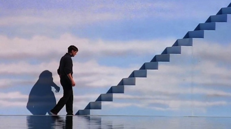 Truman walks up stairs by a wall painted with clouds in "The Truman Show" (1998)