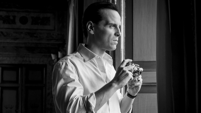 Andrew Scott as Tom Ripley, looking out a window and holding a camera, in Ripley