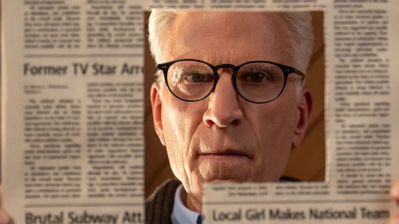 Charles looking through a news paper with a cutout hole in the shape of an article