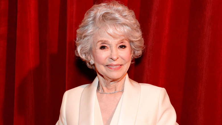 Rita Moreno posing before a red curtain