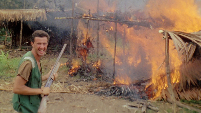 Man with gun laughs at flaming hut