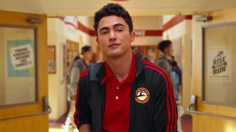 Darren Barnet as Paxton wearing a swim team jacket and walking in the school halls in Never Have I Ever