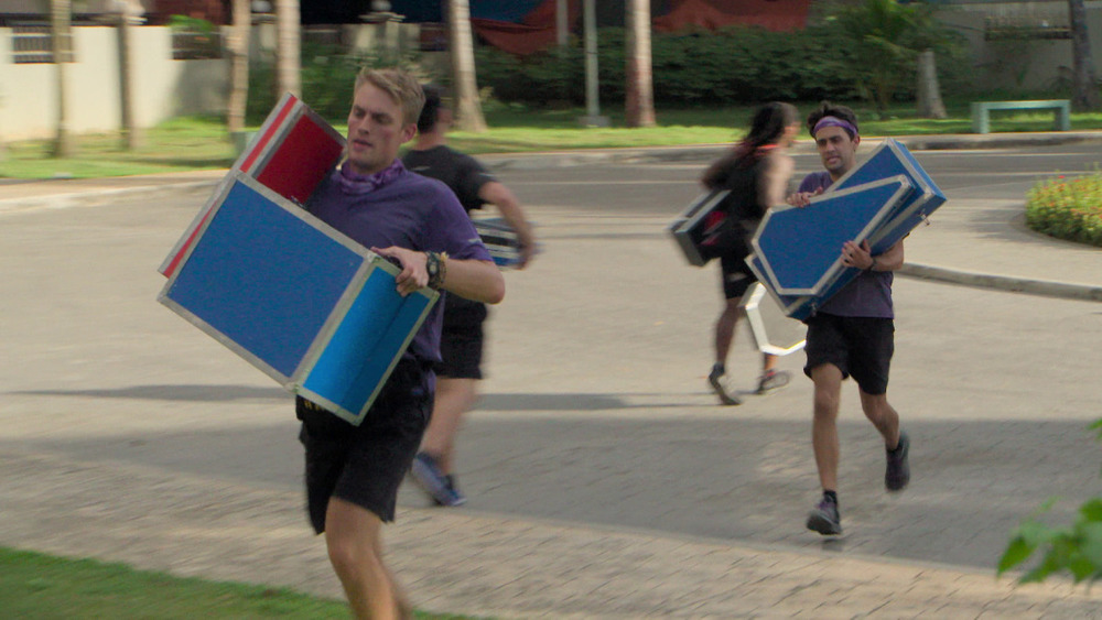 The Amazing Race teams run with boxes