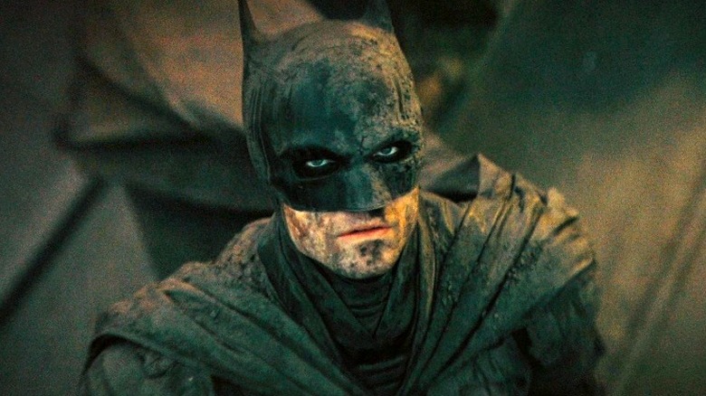 Batman stands, covered in dirt and ash