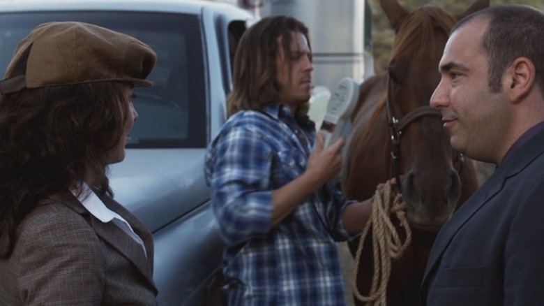 A man and woman look on as a man brushes a horse