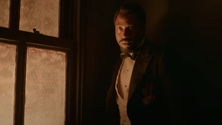 Harold stands in the dark near a lit window, wearing a tux