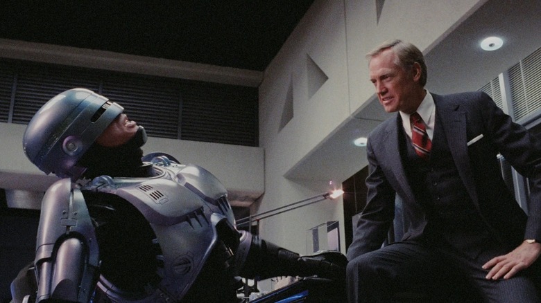 Executive seated authoritatively in front of RoboCop
