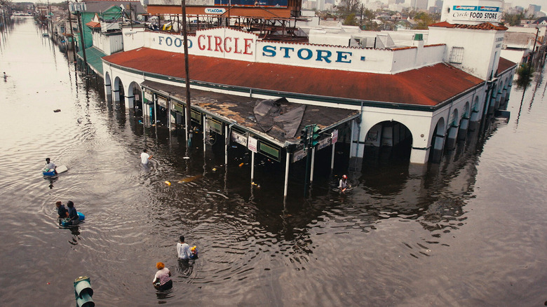 A small group of people wade through flood waters in front of a store