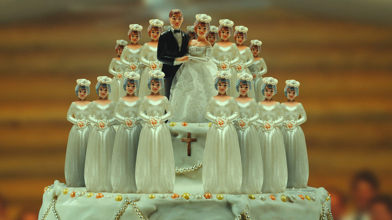 A wedding cake with one groom topper and 18 bride toppers