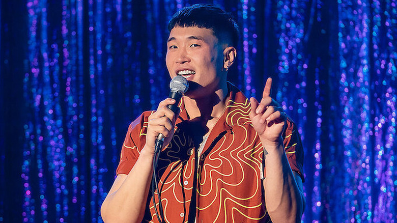 Joel Kim Booster gestures with one hand and holds the mic with the other during the filming of his stand-up special Psychosexual