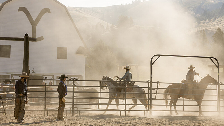 Ranchers riding their horses in front of the barn