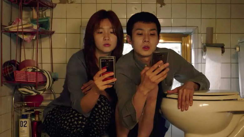 Ki-woo and Ki-jung looking at phones in bathroom