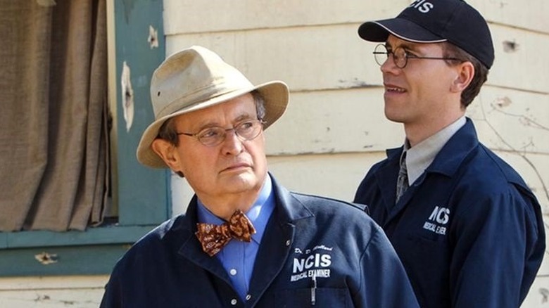 Ducky and Dr. Palmer stand near a bullet-ridden house