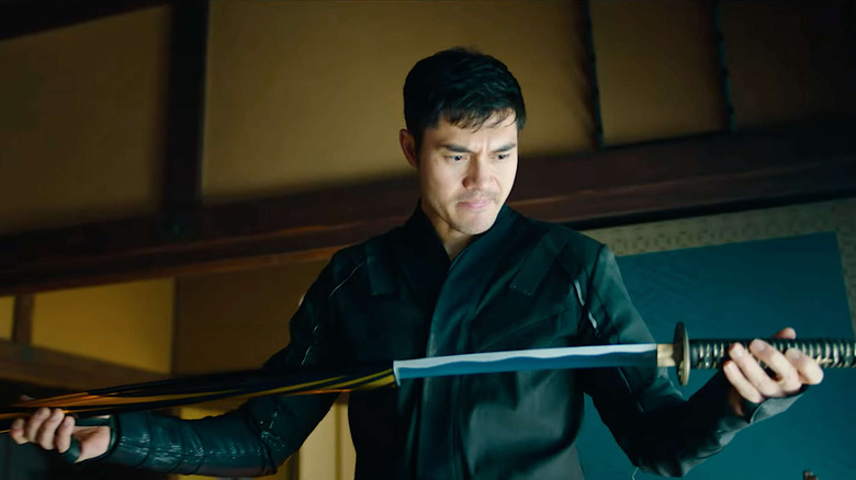 Henry Golding looking over a sword