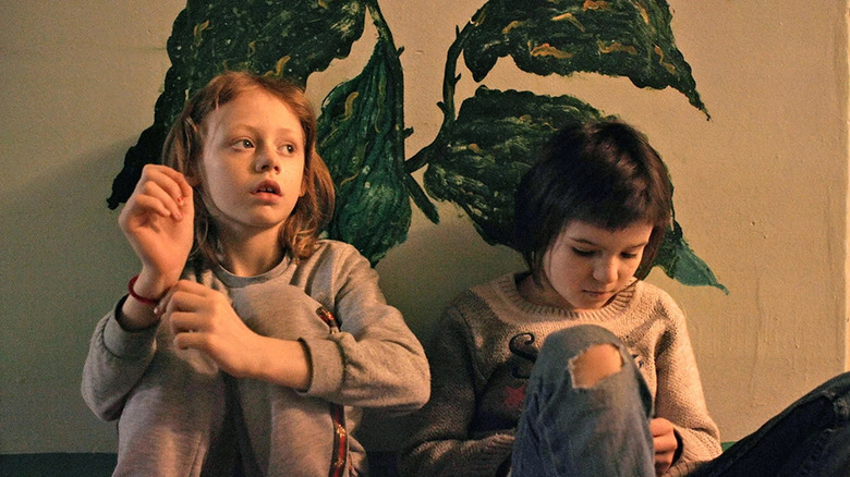 Children sit against a wall in a shelter