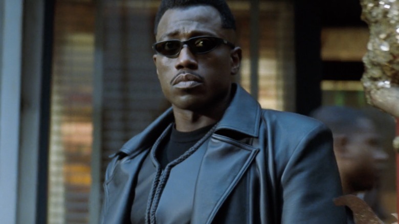 Wesley Snipes stands on a sidewalk dressed in leather with sunglasses