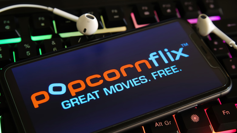 Popcornflix app on phone atop keyboard with earbuds