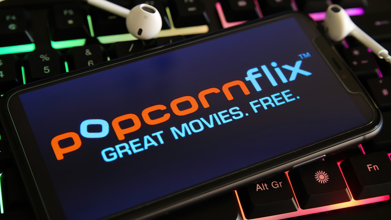 Popcornflix app on phone atop keyboard with earbuds