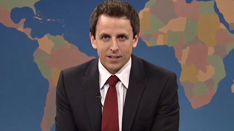 Seth Meyers sits in front of world map