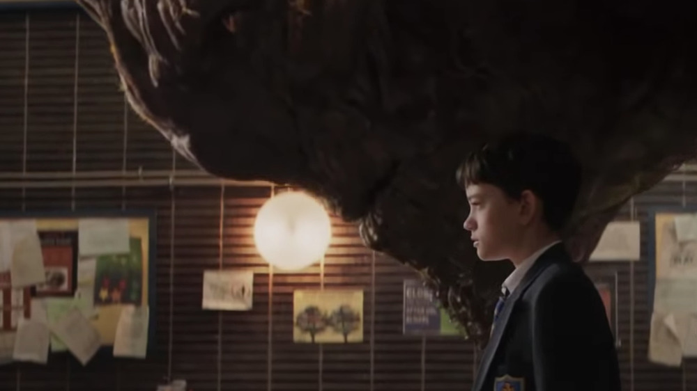 a young boy stands beside an enormous monster