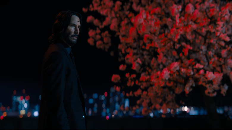 John Wick standing against red tree