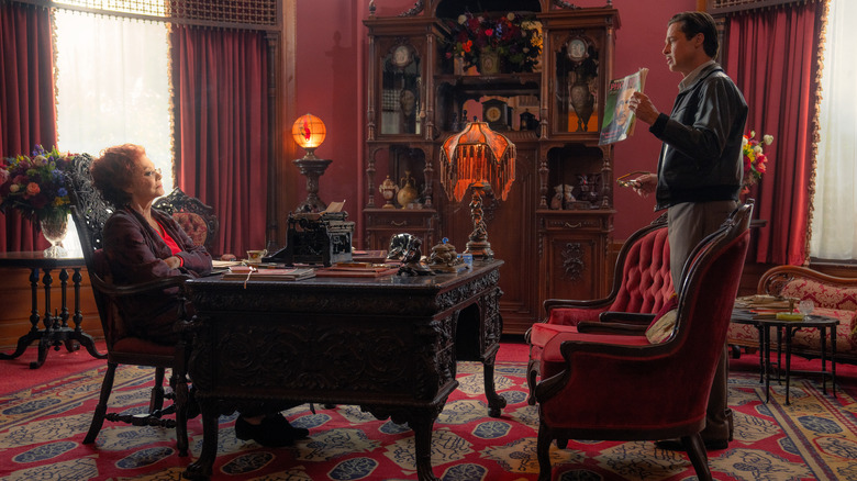 Elinor St. John sits at her desk with Jack Conrad standing in front of her with a magazine