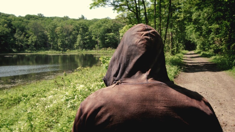 Hooded figure approaches the lake