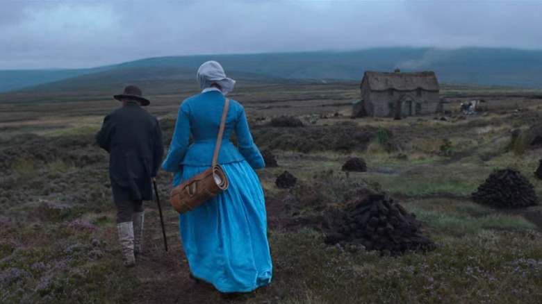 Two people in 19th century dress approach a house in the middle of a vast plain