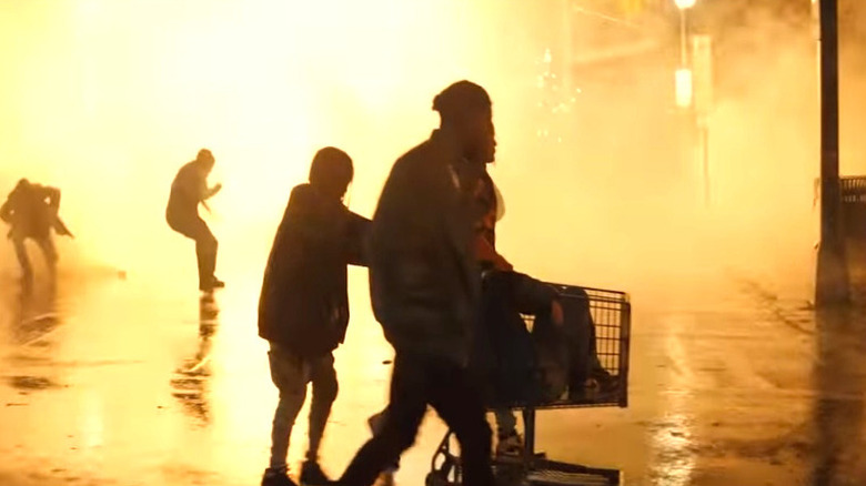 People walk down a street, silhouetted by fire