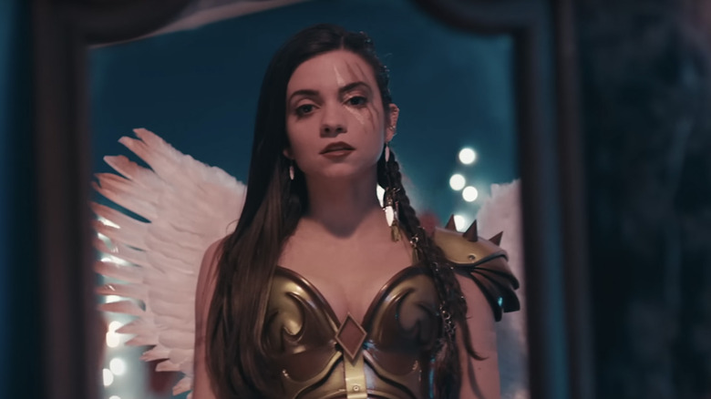 Sienna looks at herself in a mirror, wearing battle armor and angel wings