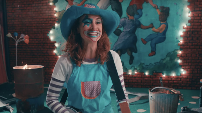 A woman dressed in cheerful clown makeup holds a guitar