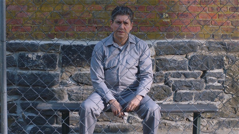 Older Joel in prison garb behind a fence