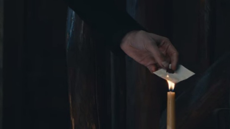 a hand holds a letter in a candle flame