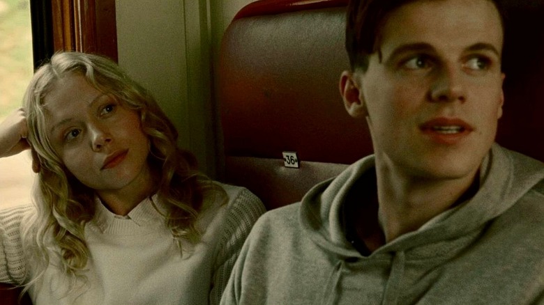 Marina and Simon riding in a train in "The Postcard Killings" (2020)