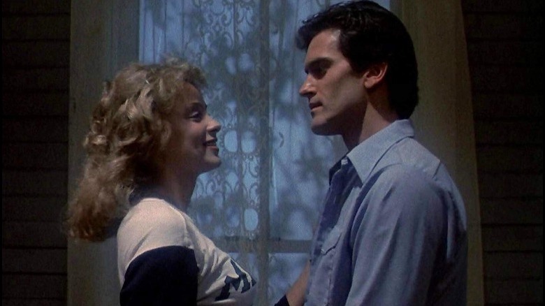 A man and a woman stand face-to-face in front of a white lace curtain