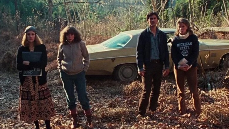 Four young people stand in front of an Oldsmobile in the woods