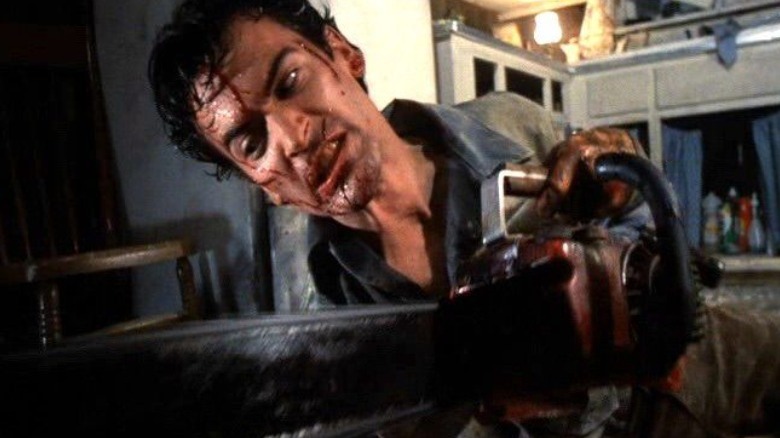 A man with blood on his face grimaces while wielding a chainsaw in a kitchen