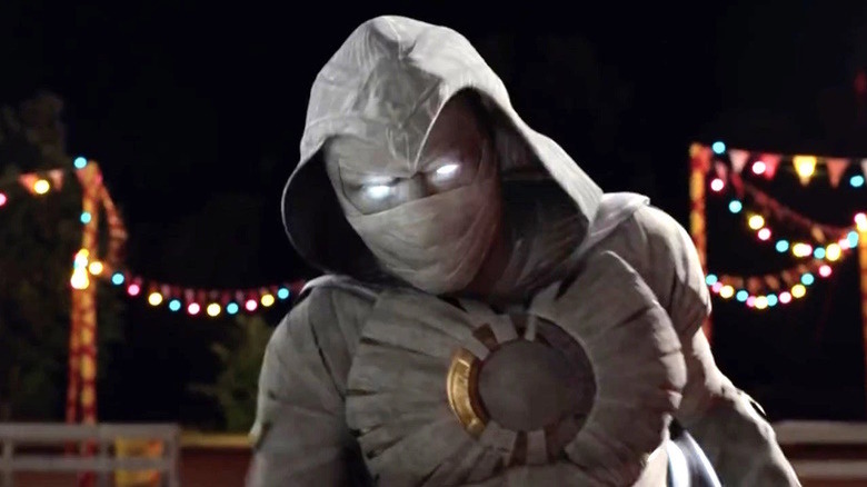 Moon Knight in costume at night with lights behind him